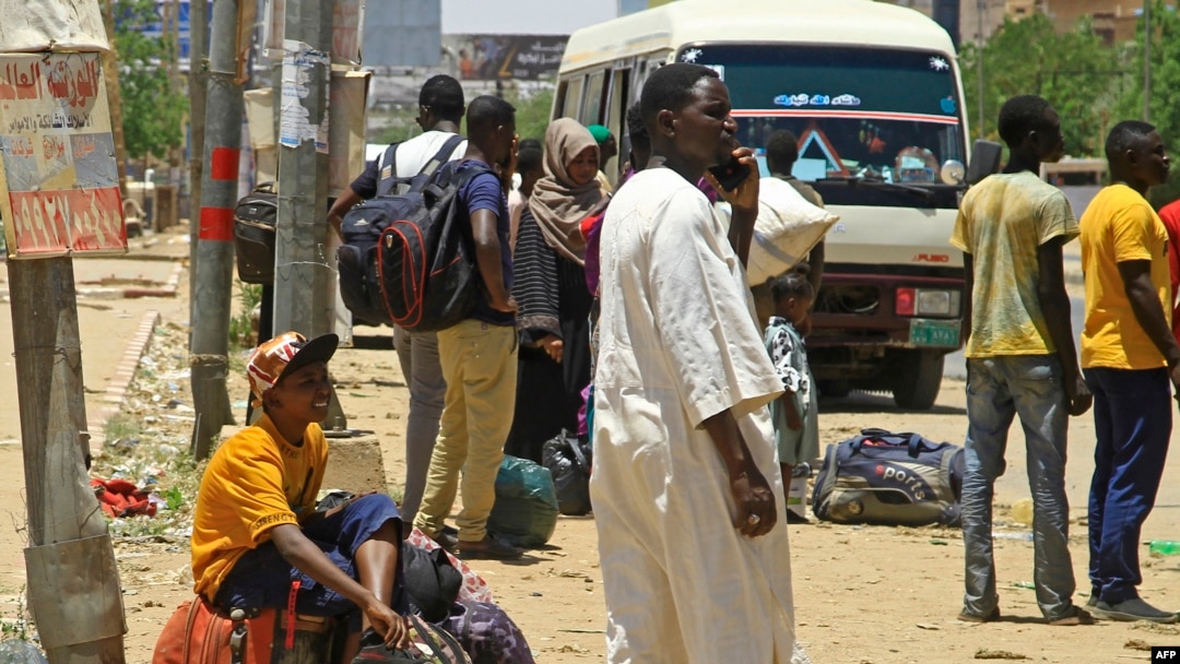 People wait for a bus to flee from southern Khartoum, Sudan, April 18, 2023, as fighting between the army and paramilitary forces led by rival generals rages for a fourth day.