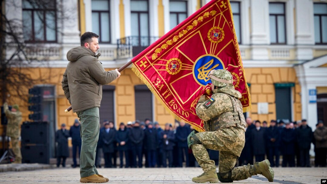 Ukrajinski predsednik Volodimir Zelenski drži zastavu vojne jedinice dok je oficir ljubi tokom komemorativnog događaja povodom godišnjice rata između Rusije i Ukrajine u Kijevu, Ukrajina, 24. februara 2023.