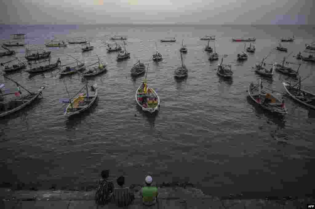 People sit next to traditional boats along the coastline in Surabaya, Indonesia.