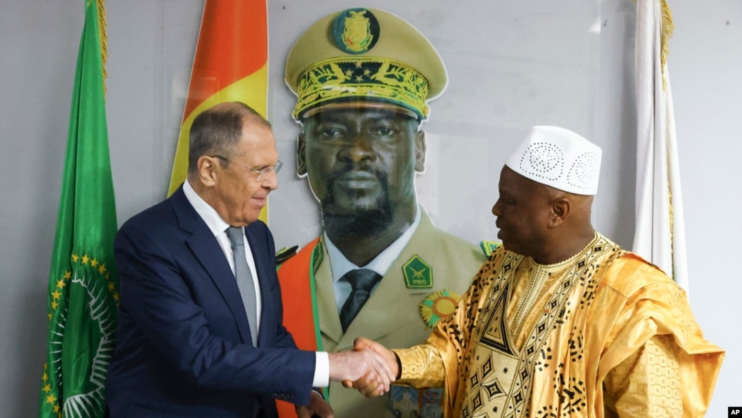 In this photo released by Russian Foreign Ministry Press Service, Russian Foreign Minister Sergey Lavrov, left, and Guinea's foreign minister Morissanda Kouyate shake hands near a portrait of Guinea's President Mamadi Doumbouya in Conakry, Guinea, on June 3, 2024.