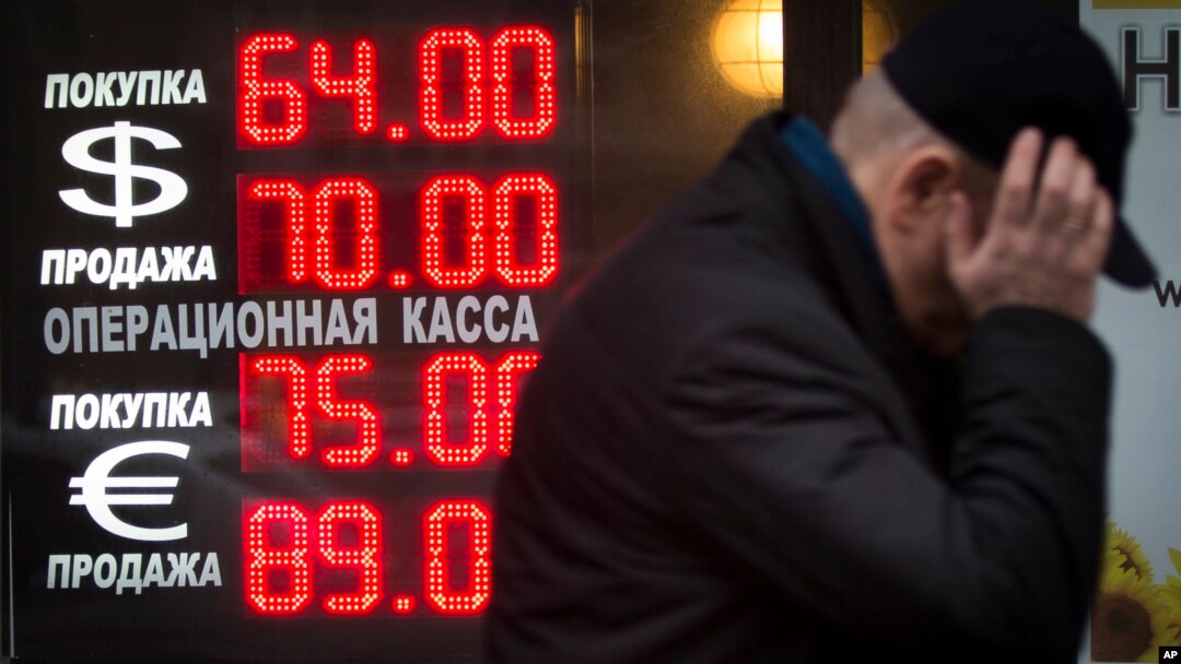 FILE - In this Dec. 16, 2014 file photo, a man walks by a sign advertising currencies of an exchange office in Moscow, Russia.