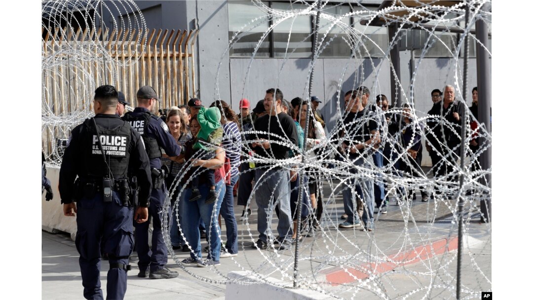 In this Nov. 19, 2018, file photo, people line up to cross into the United States from Tijuana, Mexico, seen through barriers topped with concertina wire at the San Ysidro port of entry in San Diego.