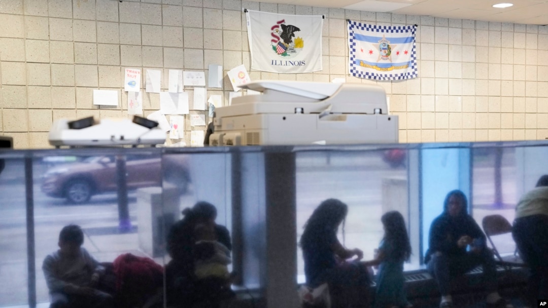 ARCHIVO - Migrantes procedentes de Venezuela se ven reflejados en una pared de mármol mientras encuentran refugio en la comisaría del distrito 16 del Departamento de Policía de Chicago el 1 de mayo de 2023. 