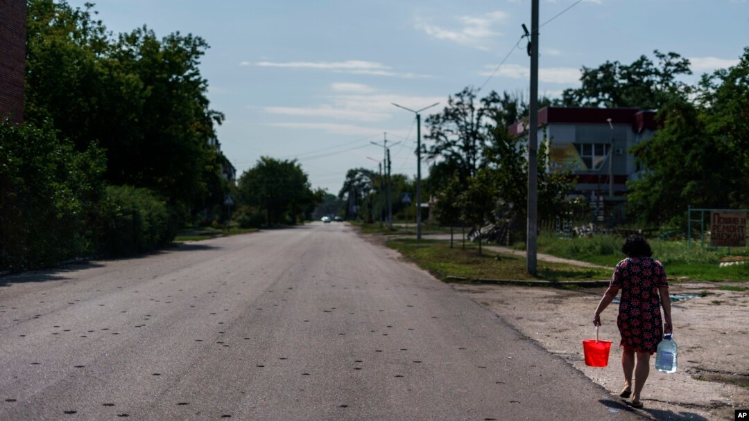 A resident carries water from a well down a road damaged by shrapnel from a May rocket attack in Sloviansk, Donetsk region, eastern Ukraine, Saturday, Aug. 6, 2022. (AP Photo/David Goldman) 