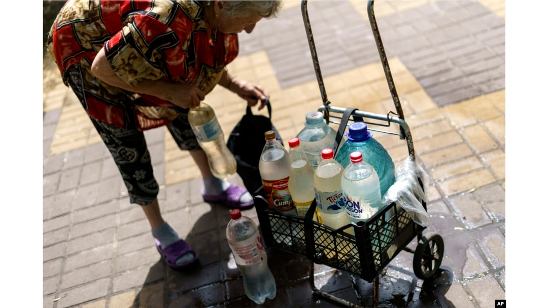 Lyubov Mahlii, 76, packs a crate with water bottles she filled up at a public tank to take back to her apartment in Sloviansk, Donetsk region, eastern Ukraine, Saturday, Aug. 6, 2022. " (AP Photo/David Goldman)