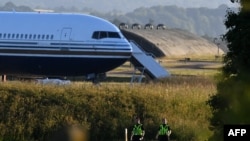 Two police officers walk near a Boeing 767 at a military base in Amesbury, Salisbury, on June 14, 2022, preparing to take asylum-seekers to Rwanda. After a last-minute intervention by the European Court of Human Rights, Britain canceled its first deportation flight.