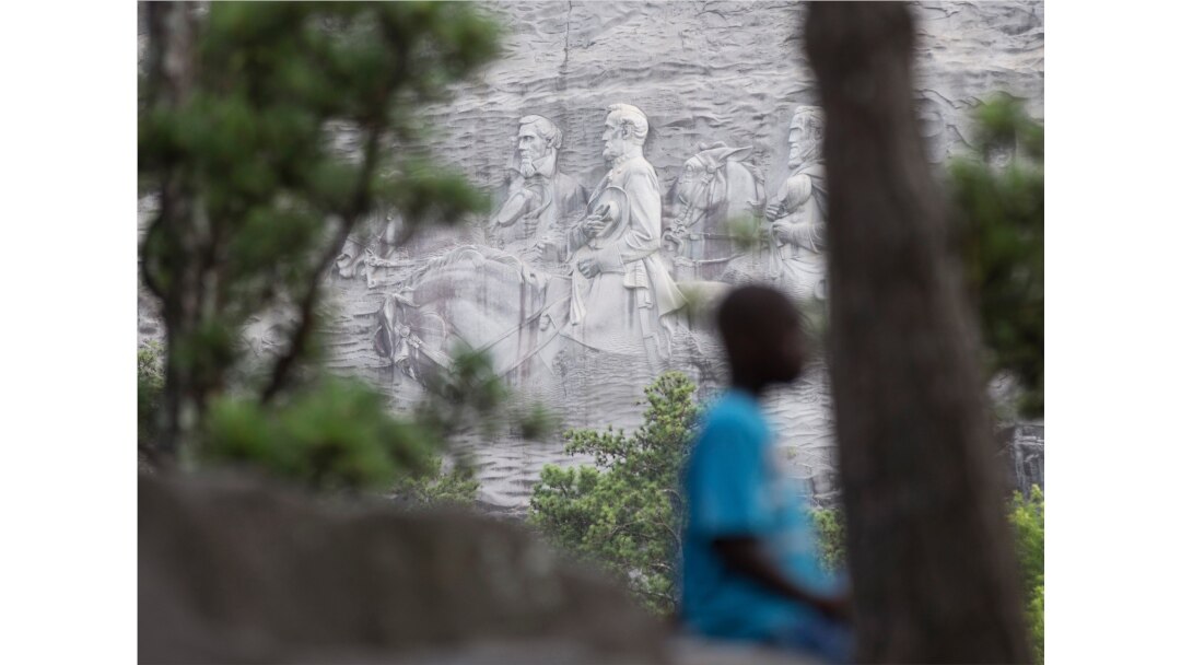 FILE - A youngster plays on a rock in front of the carving on Stone Mountain, in Stone Mountain, Ga., June 23, 2015.