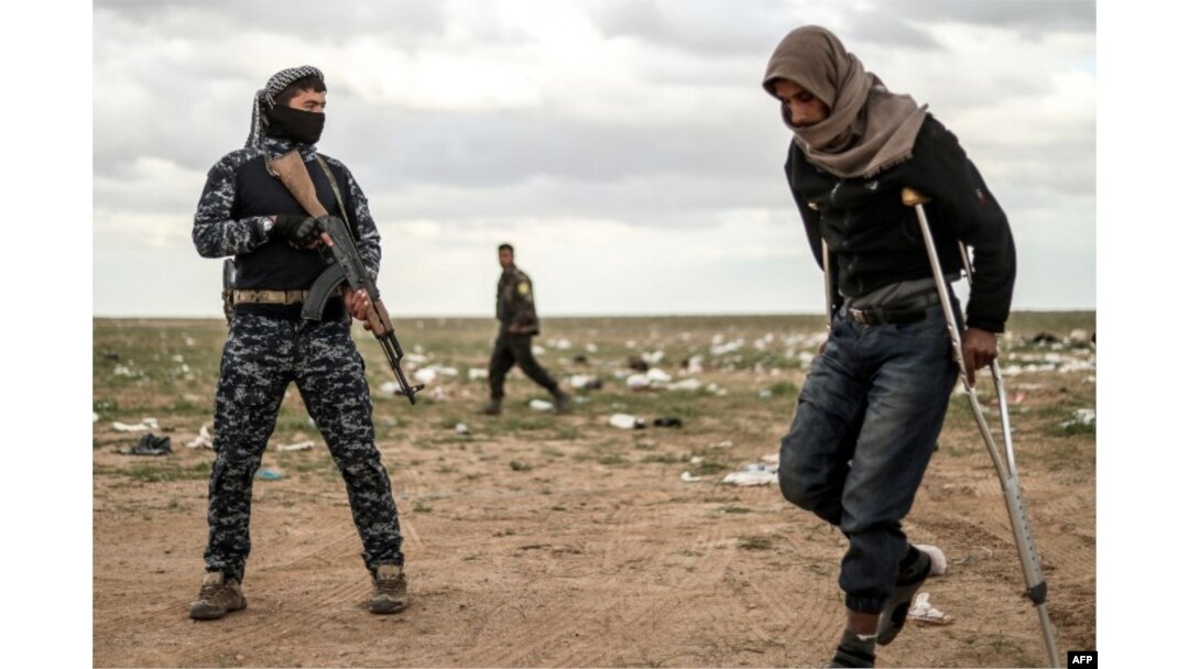 A man suspected of being an Islamic State (IS) group's fighter walks by a member of the Kurdish-led Syrian Democratic Forces (SDF) as he waits to be searched after leaving the IS group's last holdout of Baghouz, Syria, Feb. 27, 2019.
