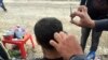 Abdullah, cutting this man's hair, does not want his face on camera for fear of IS reprisal attacks on his family inside Mosul. Refugees consistently report that their families fear death if relatives who fled talk to journalists, at the Khazir camp in Kurdish Iraq, Dec. 13, 2016. (H. Murdock/VOA)