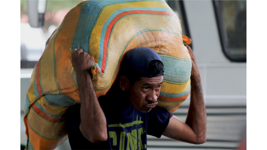 A man carries a load on his back as he works as a “lomo taxista,” or taxi of the lower back, outside a bus terminal in San Antonio, Venezuela, Sept. 19, 2019.