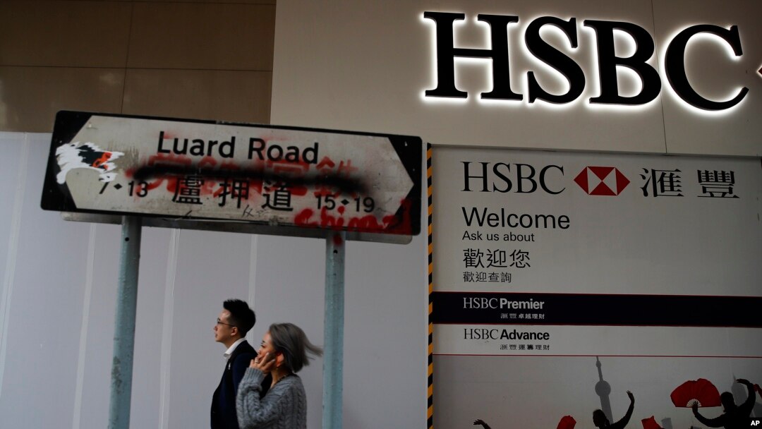 People walk by a vandalized road sign near a HSBC Bank branch covered by panels after damaged by pro-democracy protesters in Hong Kong, Jan. 4, 2020.