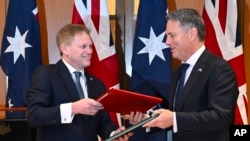 2024年3月21日，英國國防部長格蘭特·沙普斯（Grant Shapps，左）和澳洲國防部長理查德·馬勒斯（Richard Marles）在澳洲議會交換新簽署的國防和安全合作協議。