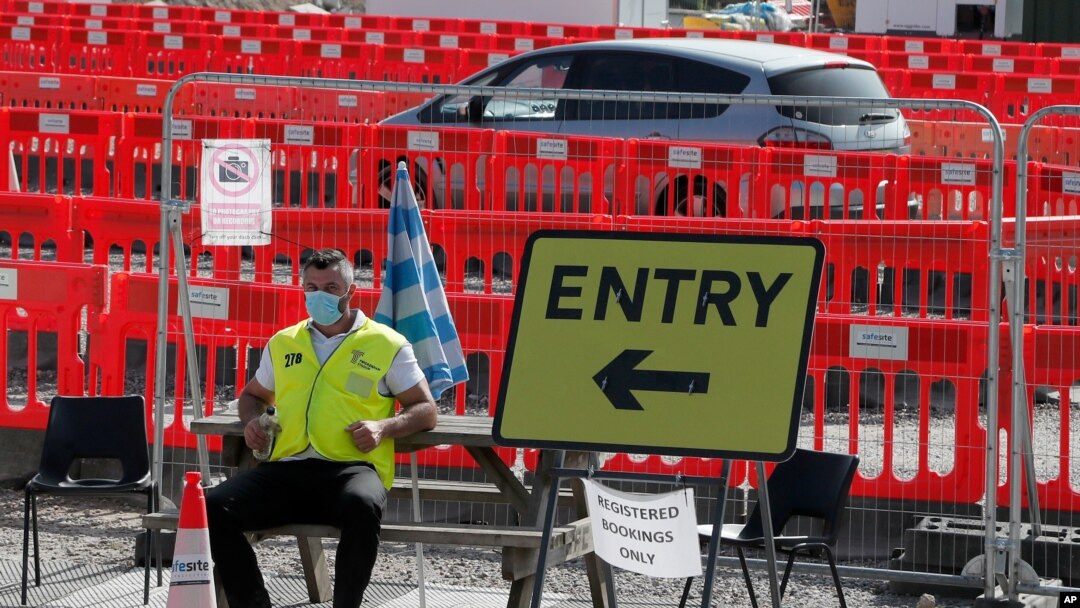 A staff member waits at the entrance to nearly empty lanes of a COVID-19 drive-thru testing facility at Twickenham stadium in London, Sept. 17, 2020. 
