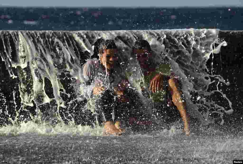 A couple laughs as a wave breaks over them on Havana's seafront boulevard 'El Malecon', Cuba, Nov. 27, 2013.