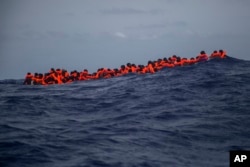 Migrants wait to be rescued in the Mediterranean Sea, about 15 miles north of Sabratha, Libya, July 25, 2017. French President Emmanuel Macron says processing asylum-seekers before their departure would save many from making the perilous journey.