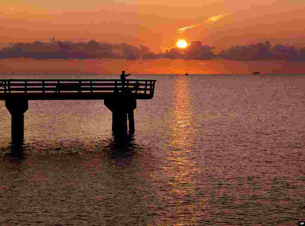 An angler stands on the pier as the sun rises In Timmendorfer Strand, Germany.