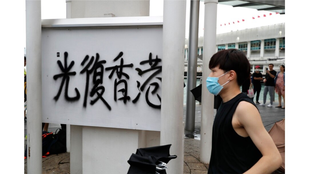 A protester walks past graffiti reading "Restore Hong Kong" during a demonstration in Hong Kong, Saturday, Aug. 3, 2019.