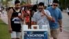 Hombres jóvenes leen las precauciones de seguridad pública mientras disfrutan de los bares y restaurantes en South Beach durante las vacaciones de primavera en medio de la pandemia del coronavirus, en Miami, el 27 de marzo de 2021.