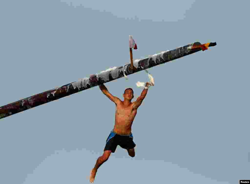 A competitor swipes lard off the "gostra", a pole covered in lard, as he falls into the sea during the celebrations of the religious feast of St Julian, patron of the town of St Julian's, Malta.