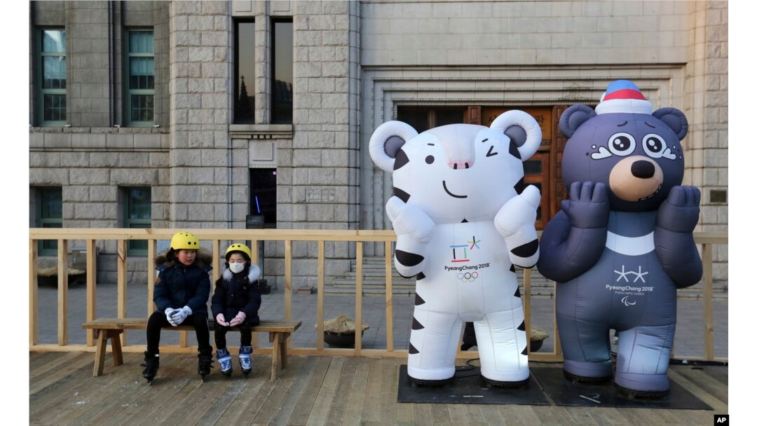 FILE - Children sit next to the 2018 Pyeongchang Winter Olympic Games' official mascots, a white tiger Soohorang, for the Olympics, and black bear Bandabi, right, for the Paralympics, near Seoul Plaza Ice Rink in Seoul, South Korea, Jan. 2, 2018.