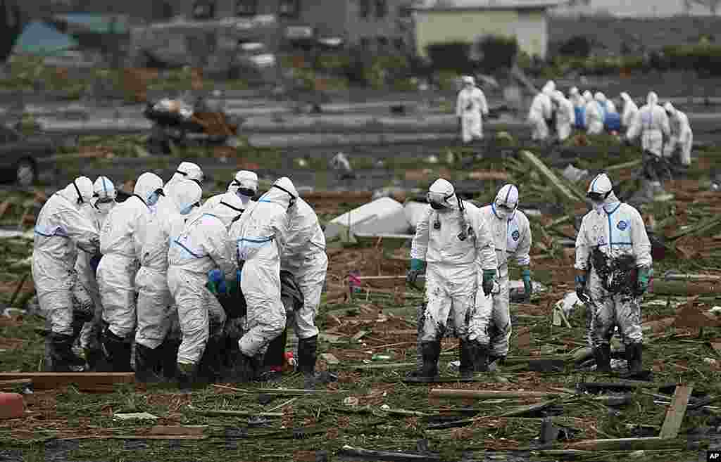 Japanese police officers wearing suits to protect them from radiation carries a victim as another group carries another body while searching for missing people in Minami Soma, Fukushima Prefecture, April 8, 2011. 