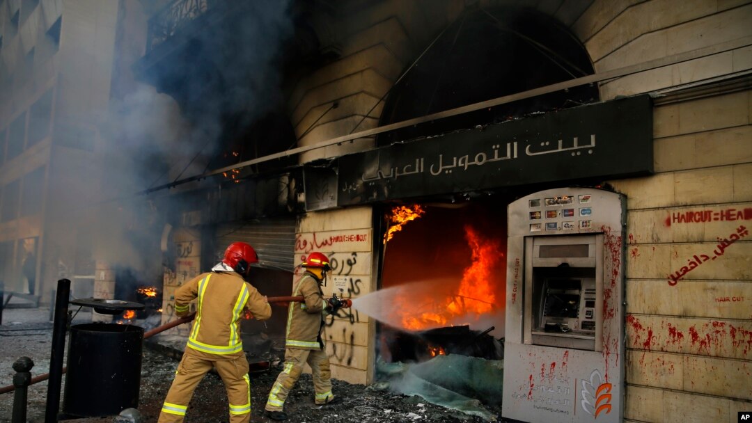 FILE - Firefighters extinguish a fire at a branch of the Credit Libanais Bank that was burnt by anti-government protesters, in the northern city of Tripoli, Lebanon, April 28, 2020.