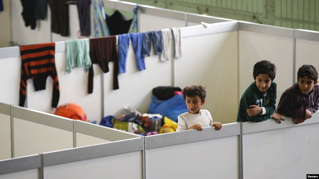 FILE - Children watch as they stand on beds in a shelter for migrants inside a hangar of the former Tempelhof airport in Berlin, Germany, Dec. 9, 2015. 