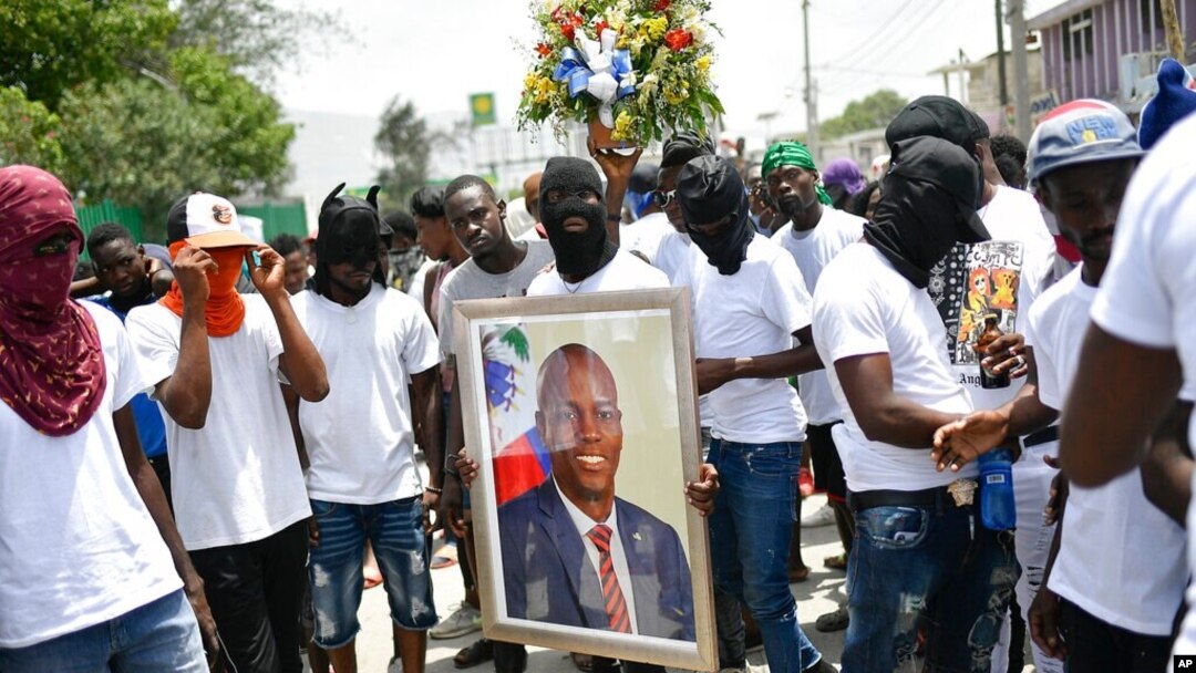 Miembros de una pandilla encabezada por Jimmy Cherizier, alias Berbecue, un expolicía que lidera una coalición de pandillas llamada "Familia G9 y Aliados", transportan un retrato del asesinado presidente Jovenel Moise durante una marcha efectuada el lunes 26 de julio de 2021.