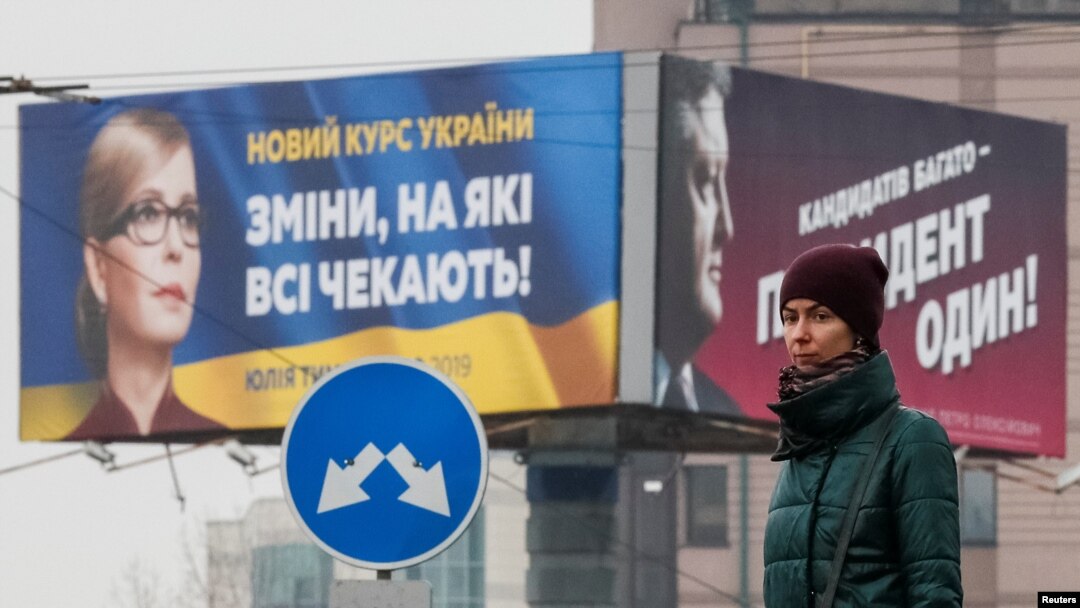 FILE - A woman stands in front of pre-election posters of opposition politician Yulia Tymoshenko and Ukrainian President Petro Poroshenko in Kyiv, Ukraine, Feb. 20, 2019. 