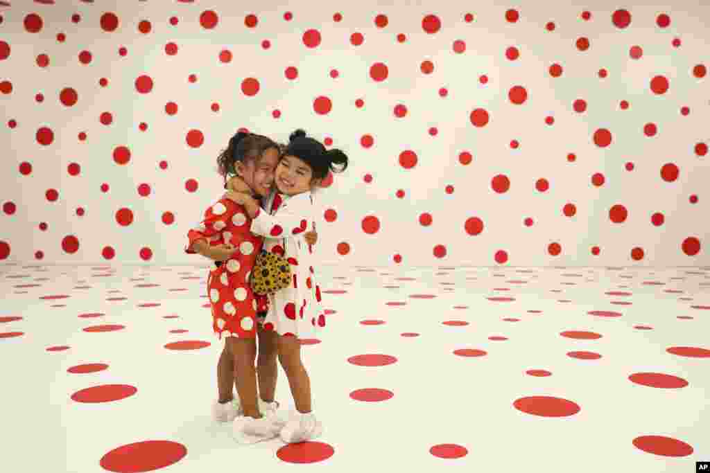 Wearing matching dresses, Takara Thomas, 3, left, and Noemi Vega, 4, hug in a polka-dotted room created by Japanese artist Yayoi Kusama, part of the installation called "With All My Love for the Tulips, I Pray Forever" at the Marciano Art Foundation in Los Angeles. 