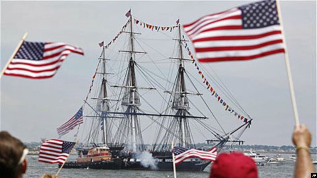 Spectators wave flags as the USS Constitution fires its cannons off Castle Island in Boston, Massachussetts, on its annual 4th of July turn-around in Boston Harbor, July 4, 2011