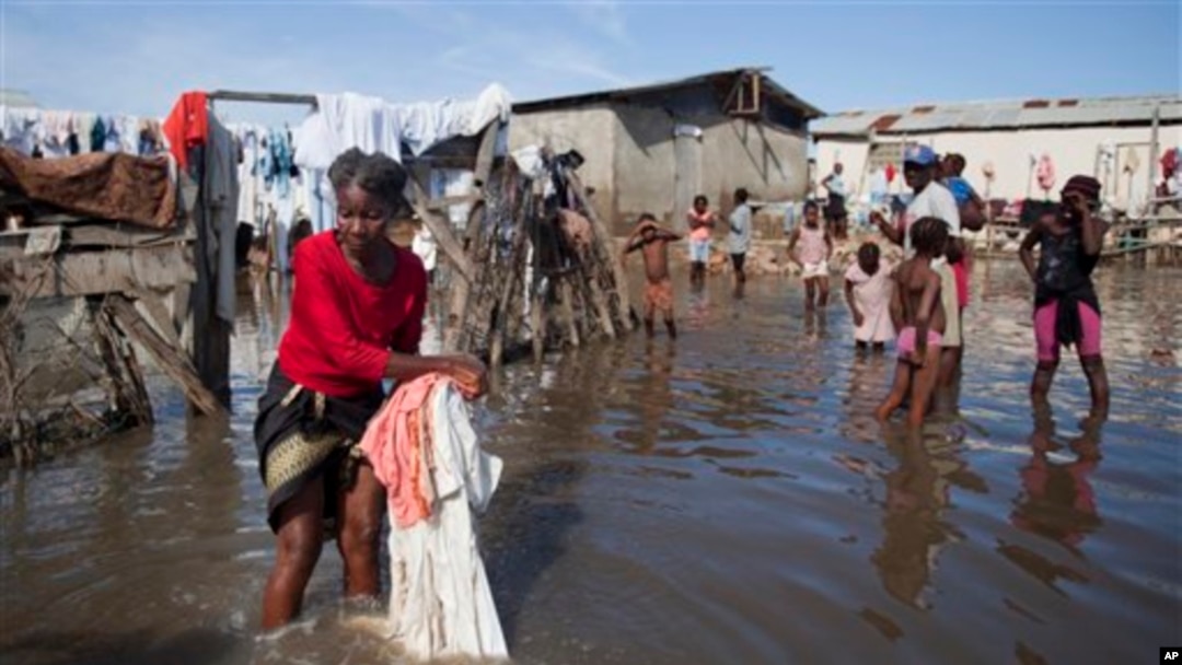 Bernard Sylphanie cleans her belongings in floodwater outside her home in Cap-Haitien, Haiti, Friday, Nov. 7, 2014. Thousands of families in Haiti and the neighboring Dominican Republic have been affected by floods from a storm system that drenched the countries for several days. At least five people were killed and one was missing. Floods raise the risk of cholera and dysentery outbreaks. (AP Photo/Dieu Nalio Chery)