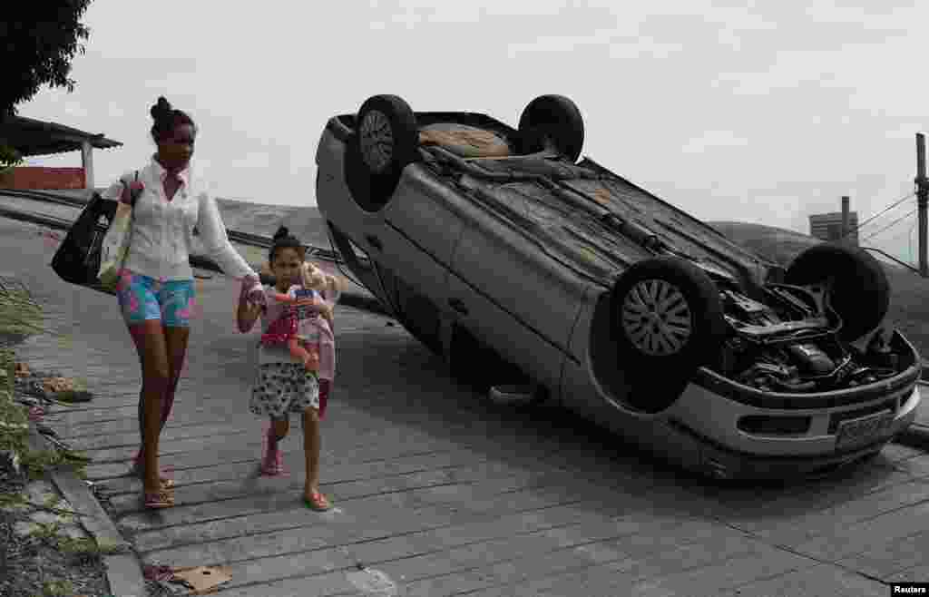 Residents walk past a car, which according to its owner was damaged during violent clashes between policemen and drug gangs during an operation in Sao Carlos slums complex in Rio de Janeiro, Brazil, Aug. 28, 2018.