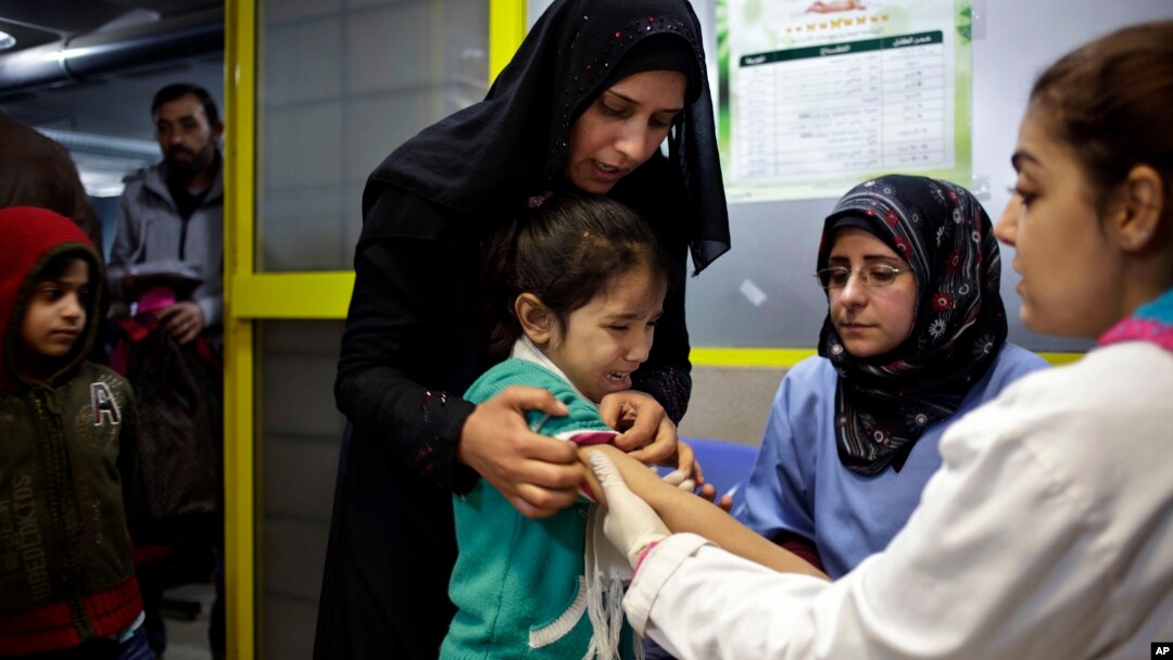 A Syrian girl cries after receiving the measles vaccine from UNICEF nurses Nadine Houjairi (2nd R), and Genivieve Bashalani (R) at the U.N. refugee agency's registration center in Zahleh, in Lebanon's Bekaa Valley, Dec. 18, 2013.