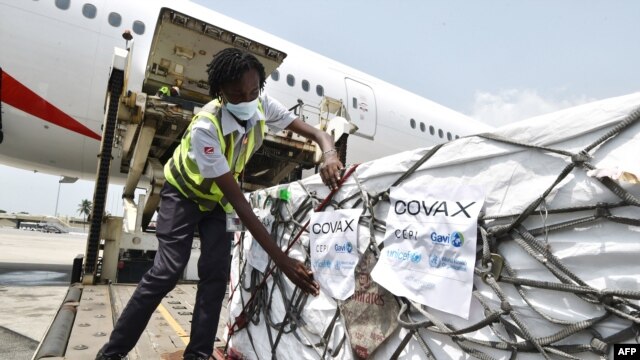 FILE - A woman attaches COVAX stickers to a shipment of AstraZeneca Covid-19 vaccine from a plane at Felix Houphouet Boigny airport of Abidjan on Feb. 26, 2021.
