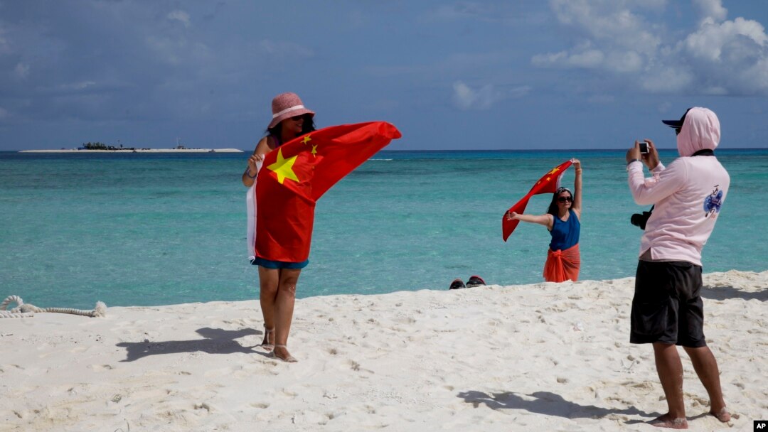 FILE - Chinese tourists take souvenir photos with the Chinese national flag as they visit Quanfu Island, one of Paracel Islands of Sansha prefecture of southern China's Hainan province in the South China Sea, Sept. 14, 2014. 