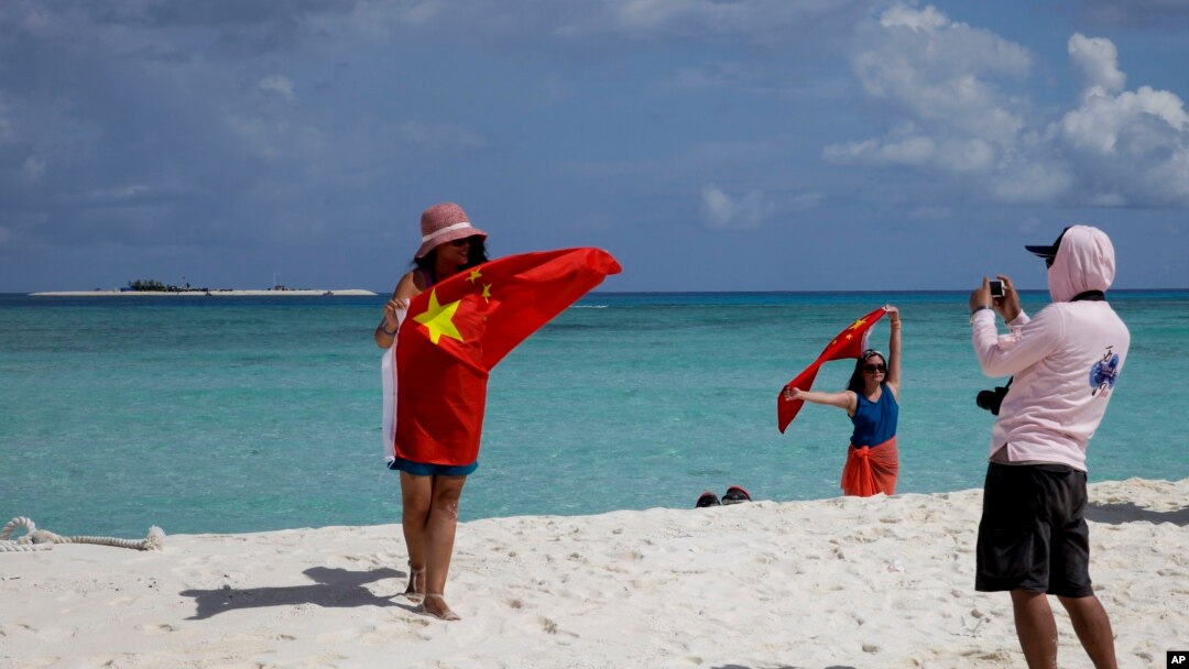 FILE - Chinese tourists take souvenir photos with the Chinese national flag as they visit Quanfu Island, one of Paracel Islands of Sansha prefecture of southern China's Hainan province in the South China Sea, Sept. 14, 2014. 