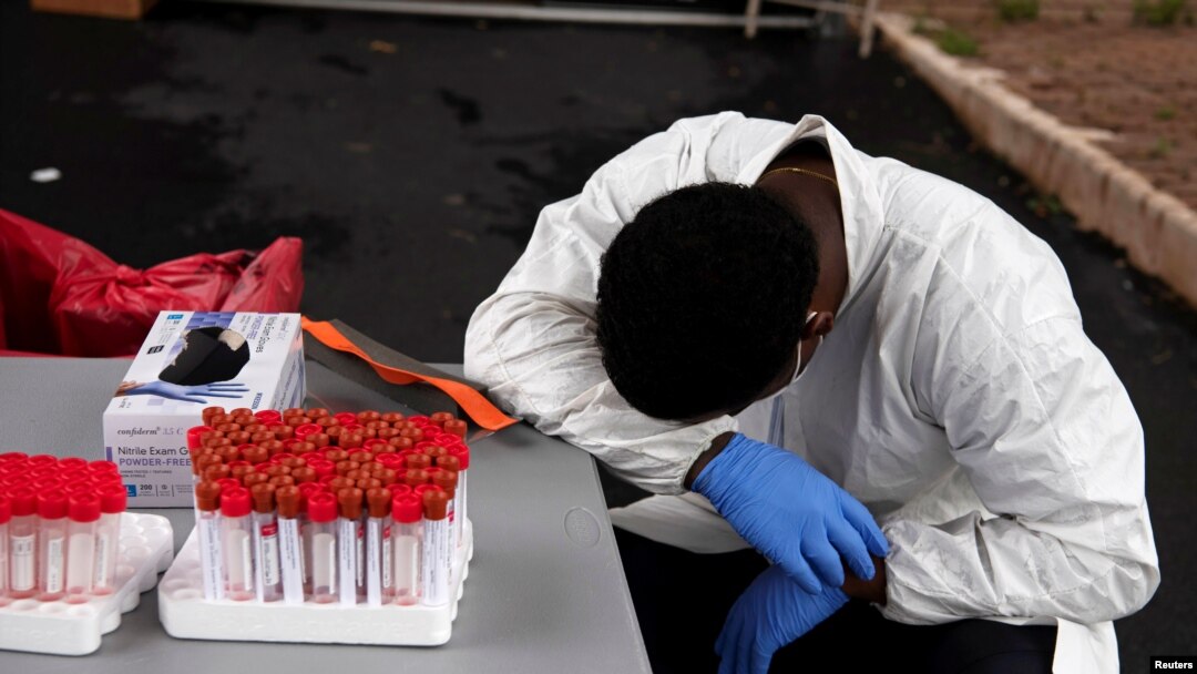 FILE - A health care worker takes a break as people wait in their vehicles in long lines for coronavirus testing in Houston, Texas, July 7, 2020. 