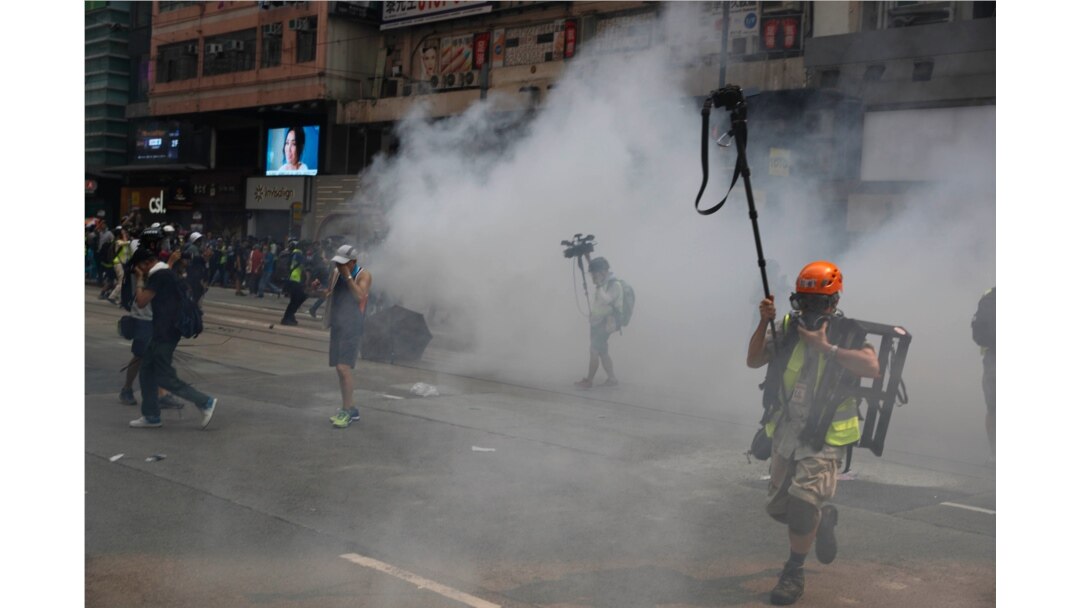 FILE - Journalists make their way through tear gas in Hong Kong, Sept. 29, 2019.