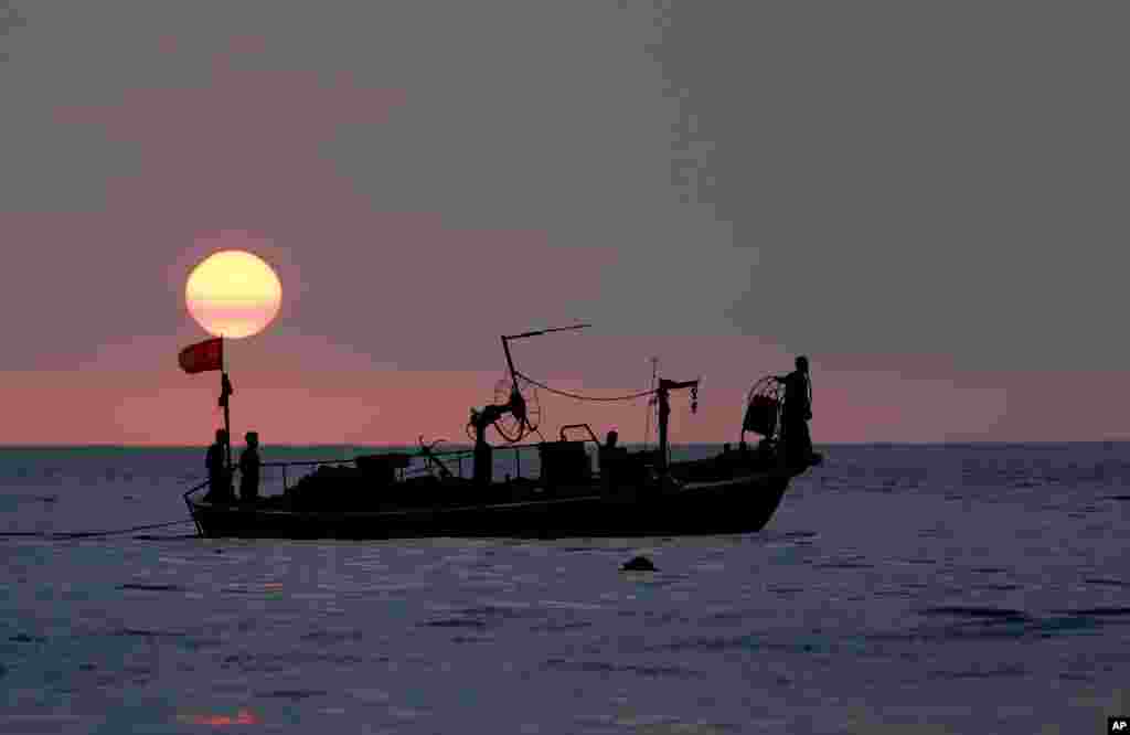 Fishermen sit at the bow of a fishing boat, in the Mediterranean Sea as the sun sets, at Ramlet al-Baida public beach, in Beirut, Lebanon.