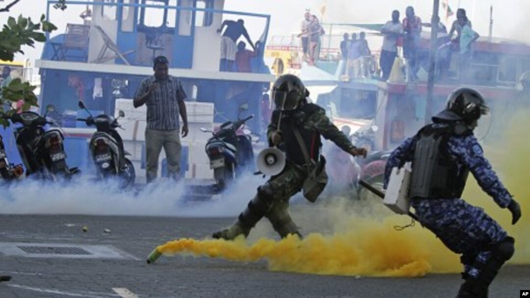 A Maldivian army soldier, left, and policeman take cover as a supporter of Mohamed Nasheed, who resigned Tuesday from his post as Maldivian President, hurls back a tear gas canister thrown during a protest in Male, Maldives, February 8, 2012.