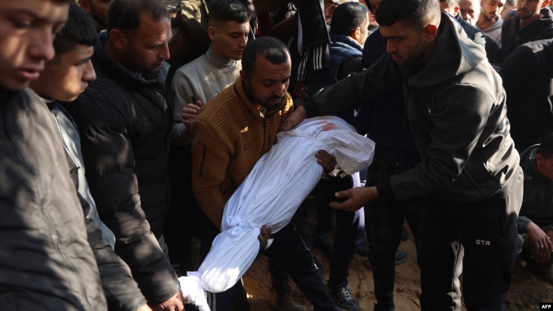 Um homem palestiniano é ajudado a colocar um corpo coberto no chão durante o funeral dos palestinianos mortos num ataque israelita na noite anterior, em Jabalia, no norte da Faixa de Gaza, a 21 de dezembro de 2024