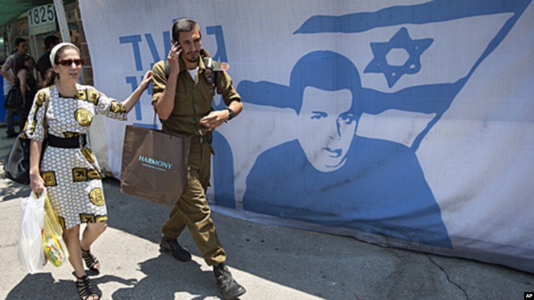 An Israeli soldier and a woman walk past a protest tent near the Prime Minister's residence, in Jerusalem, calling for the release of captured Israeli soldier Gilad Schalit, June 24, 2011.