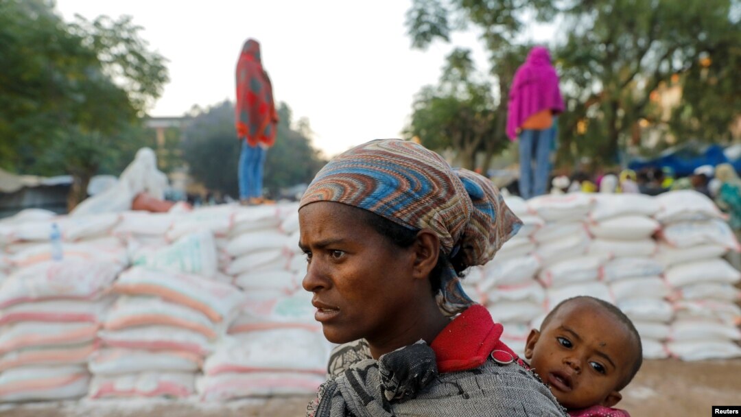 FILE - A woman carries an infant as she queues in line for food, at the Tsehaye primary school, which was turned into a temporary shelter for people displaced by conflict, in the town of Shire, Tigray region, Ethiopia, March 15, 2021.