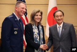 FILE - U.S. Ambassador to Japan Caroline Kennedy, center, accompanied by Lt. Gen. John Dolan, left, commander of U.S. Forces Japan, shakes hands with Japanese Chief Cabinet Secretary Yoshihide Suga after their joint press conference in Tokyo.