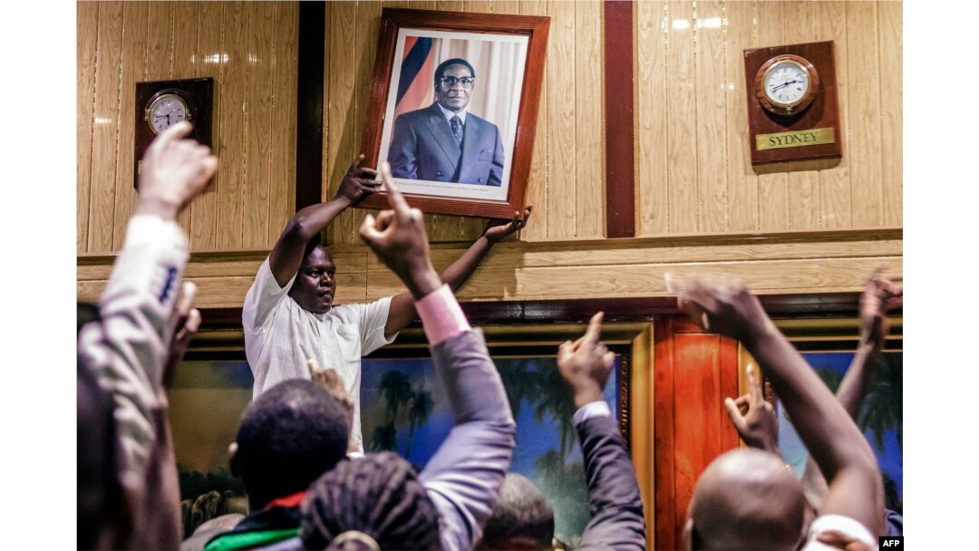 People remove from the wall at the International Conference center, where parliament had their sitting, the portrait of former Zimbabwean President Robert Mugabe after his resignation, Nov. 21, 2017, in Harare.