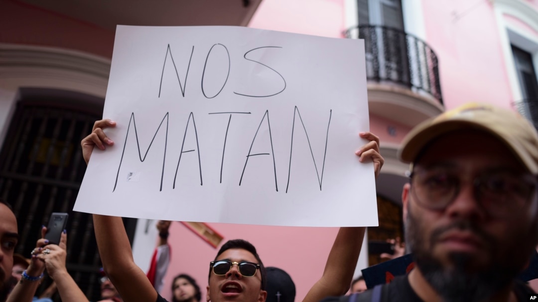 A man holds a sign that reads in Spanish "They are killing us" while demanding the resignation of Governor Wanda Vazquez after the discovery of an old warehouse filled with unused emergency supplies in San Juan, Puerto Rico, Jan. 20, 2020.