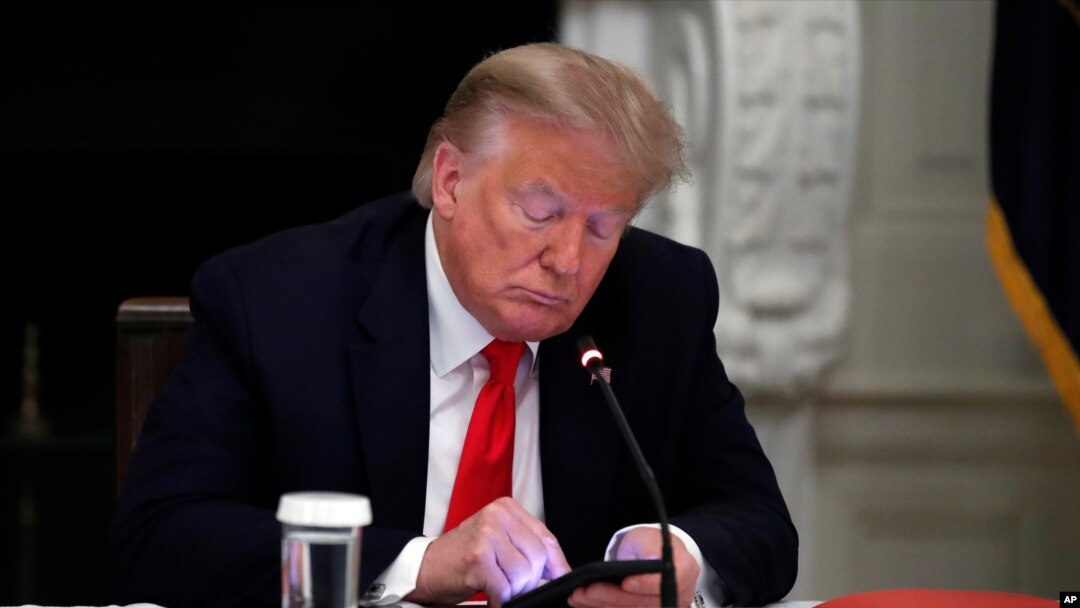 FILE - President Donald Trump checks his phone during a meeting in the State Dining Room of the White House, in Washington, June 18, 2020.