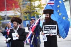 FILE - Two men wearing Orthodox Jewish attire hold placards and leaflets in support of Labor Party leader Jeremy Corbyn outside the party's conference in Liverpool, Britain, Sept. 26, 2018.