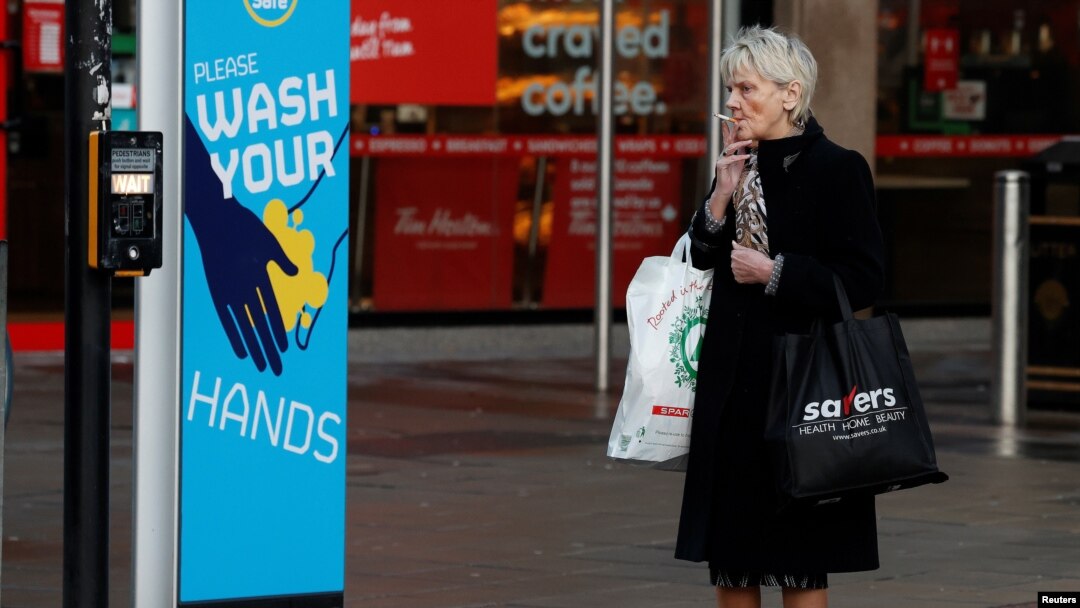 A woman smokes a cigarette as she stands by a sign encouraging people to wash their hands amid the outbreak of the coronavirus disease (COVID-19) in Belfast, Northern Ireland Jan. 2, 2021.